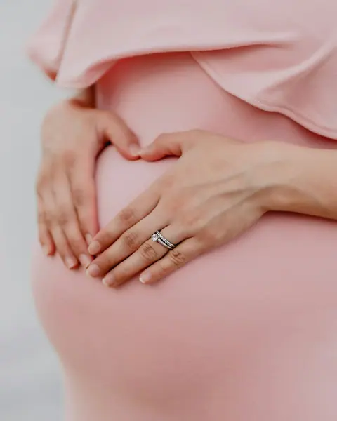 An expecting mother making a heart shape with her hands over her belly